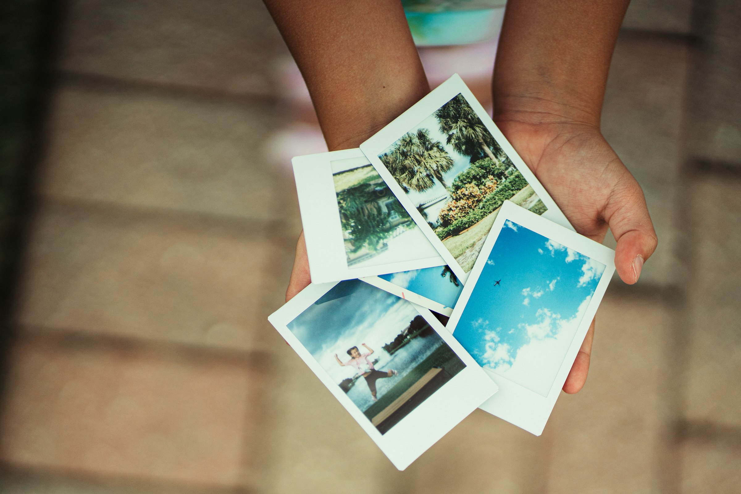 Roke držijo štiri natisnjene polaroid fotografije s poletnimi motivi